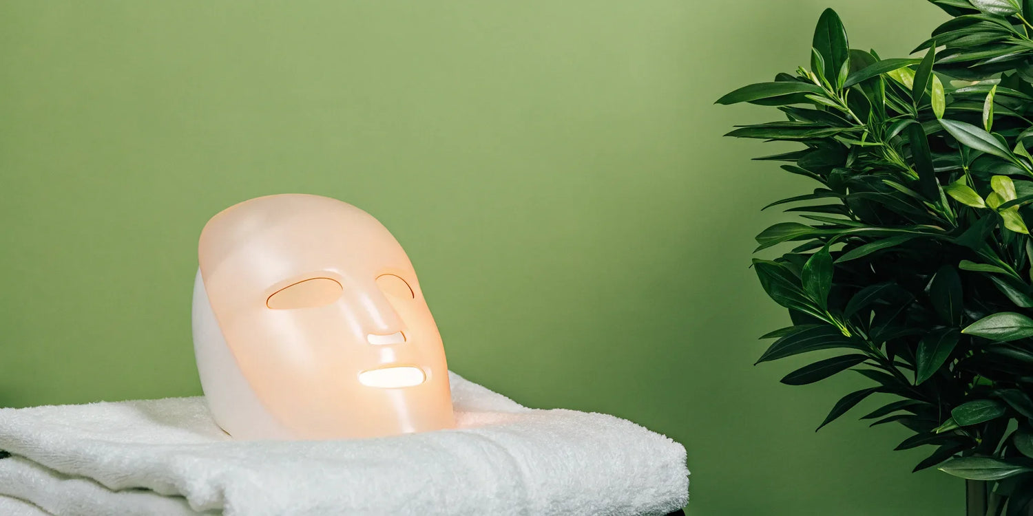 LED face and neck mask on white towels.